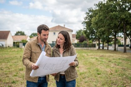 Couple examinant des plans architecturaux sur un terrain à bâtir vide dans un quartier résidentiel de Nantes