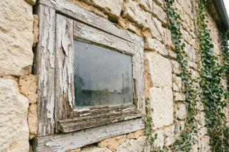 Fenêtre ancienne en bois avec peinture écaillée et joints de maçonnerie dégradés sur façade en pierre d'une vieille maison de campagne